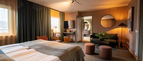 Quarto de hotel moderno com uma cama grande, uma escrivaninha, um sofá e um espelho redondo.