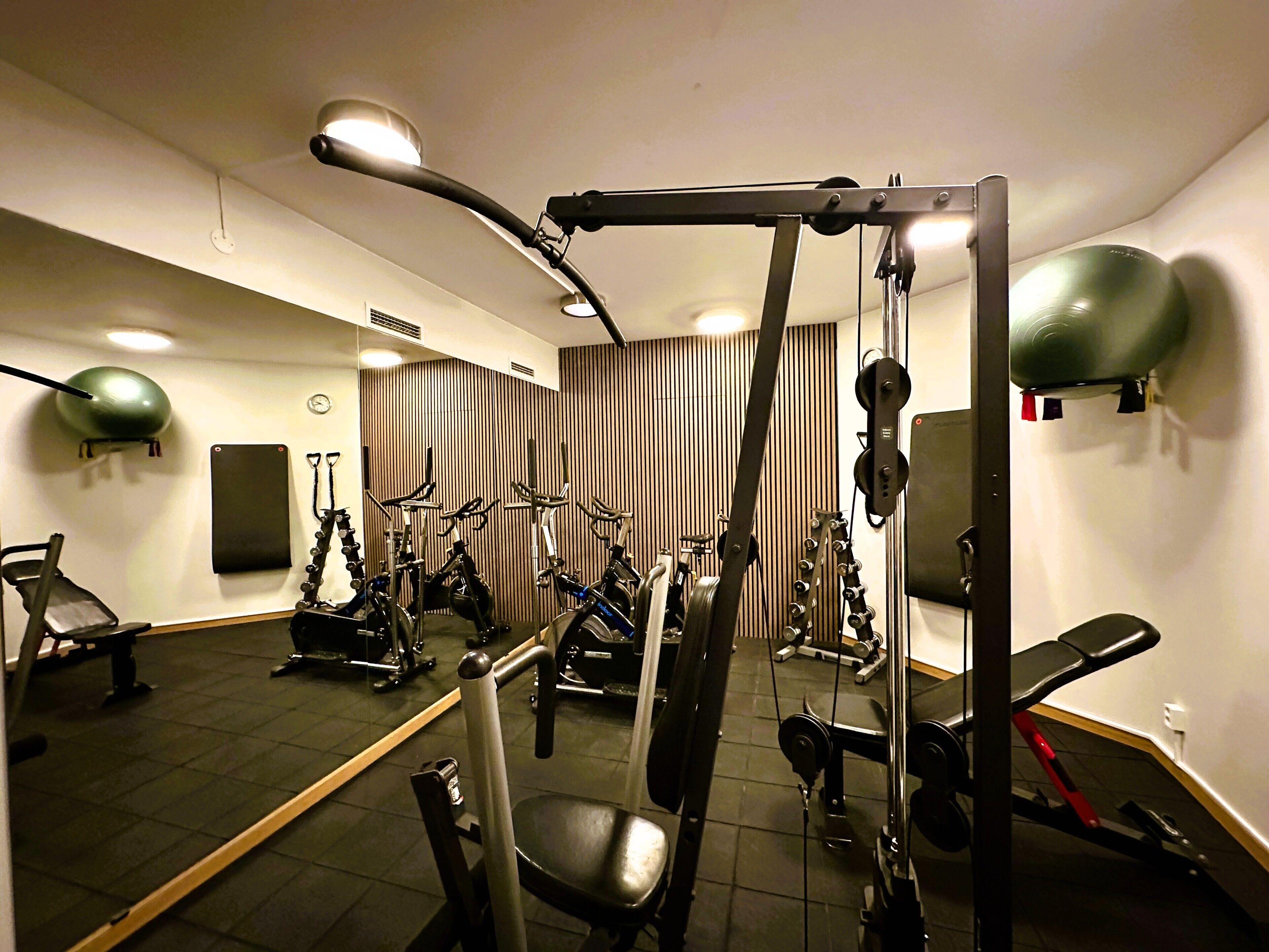 Une salle de sport équipée de matériel d’exercice, avec un miroir et une horloge au mur.