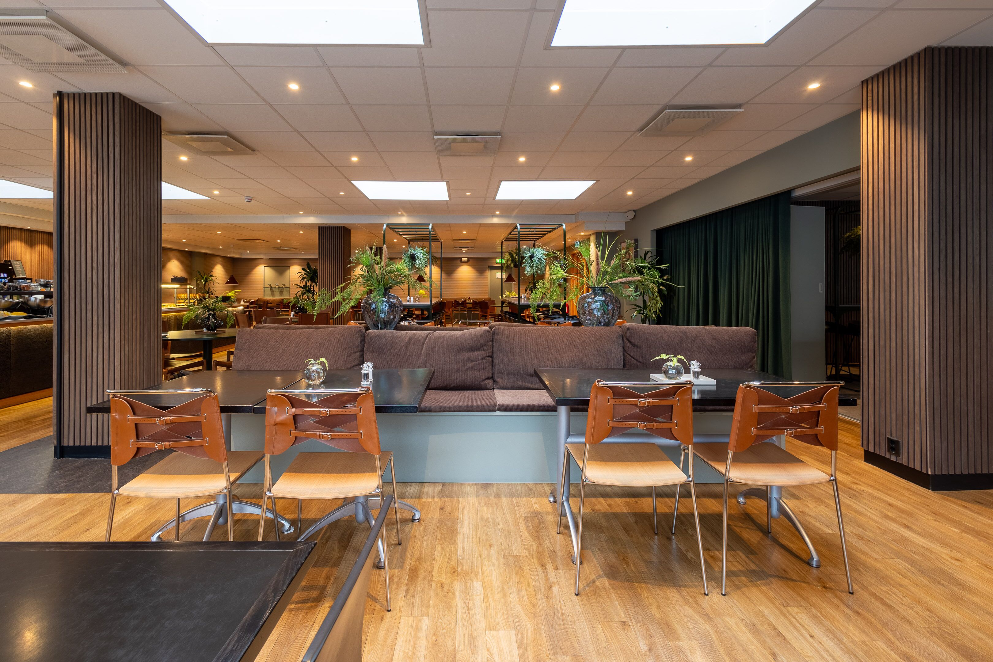 A modern lobby with a central seating area, wooden flooring, and a high ceiling with skylights.