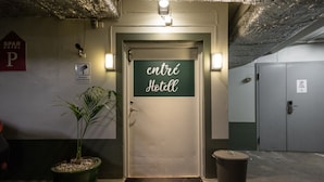A hotel entrance with a sign reading "entrée Hotel," a parking sign, a potted plant, and a trash bin. - Spar Hotel Gårda (Gothenburg)
