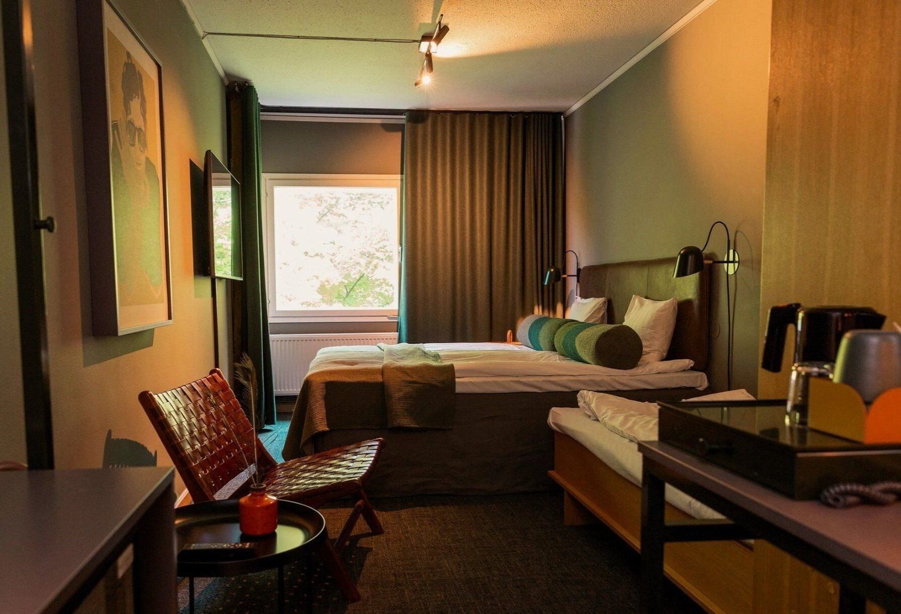 A hotel room with a bed, a desk, a chair, a table, a lamp, and a window.