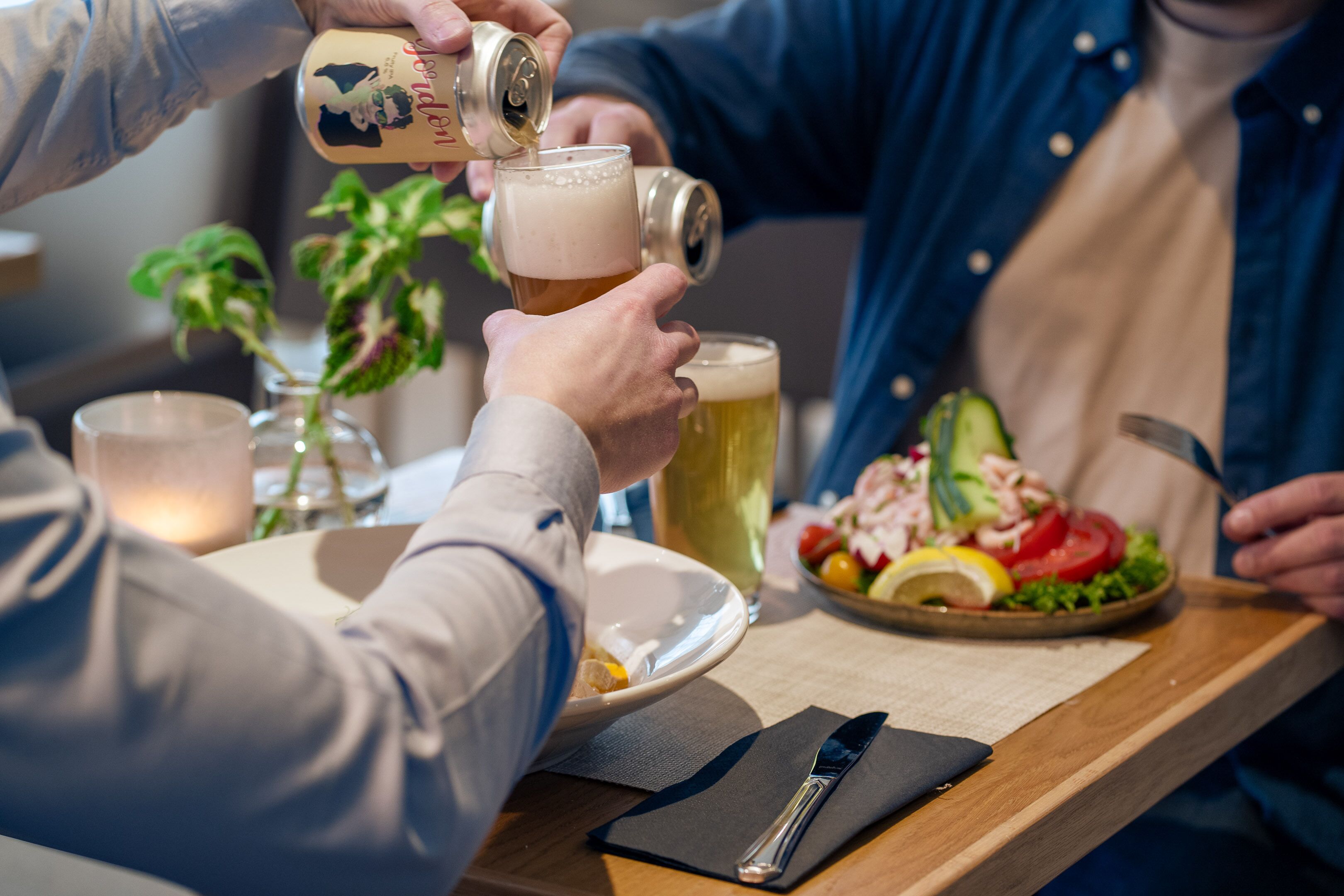 A person pouring beer into a glass, a plate of food, and a knife on a table.