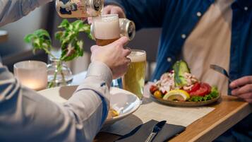 A person pouring beer into a glass, a plate of food, and a knife on a table.