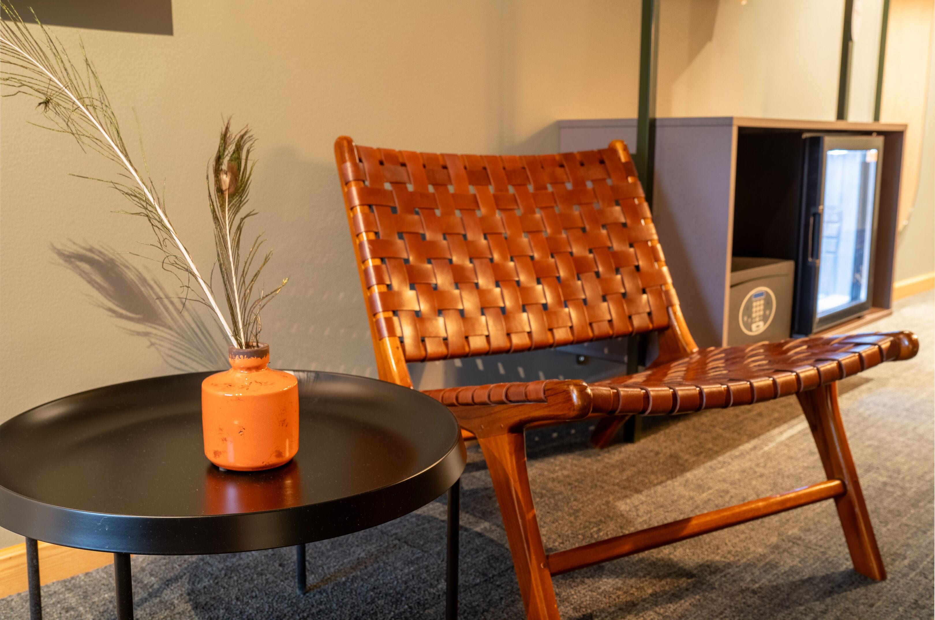 Une chaise en osier avec un coussin noir, un petit vase orange contenant des plantes séchées et une table noire.
