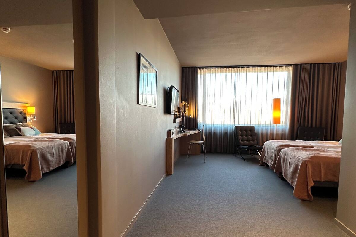 Habitació d'hotel amb dos llits, una taula de treball, una cadira, una televisió i un mirall gran.