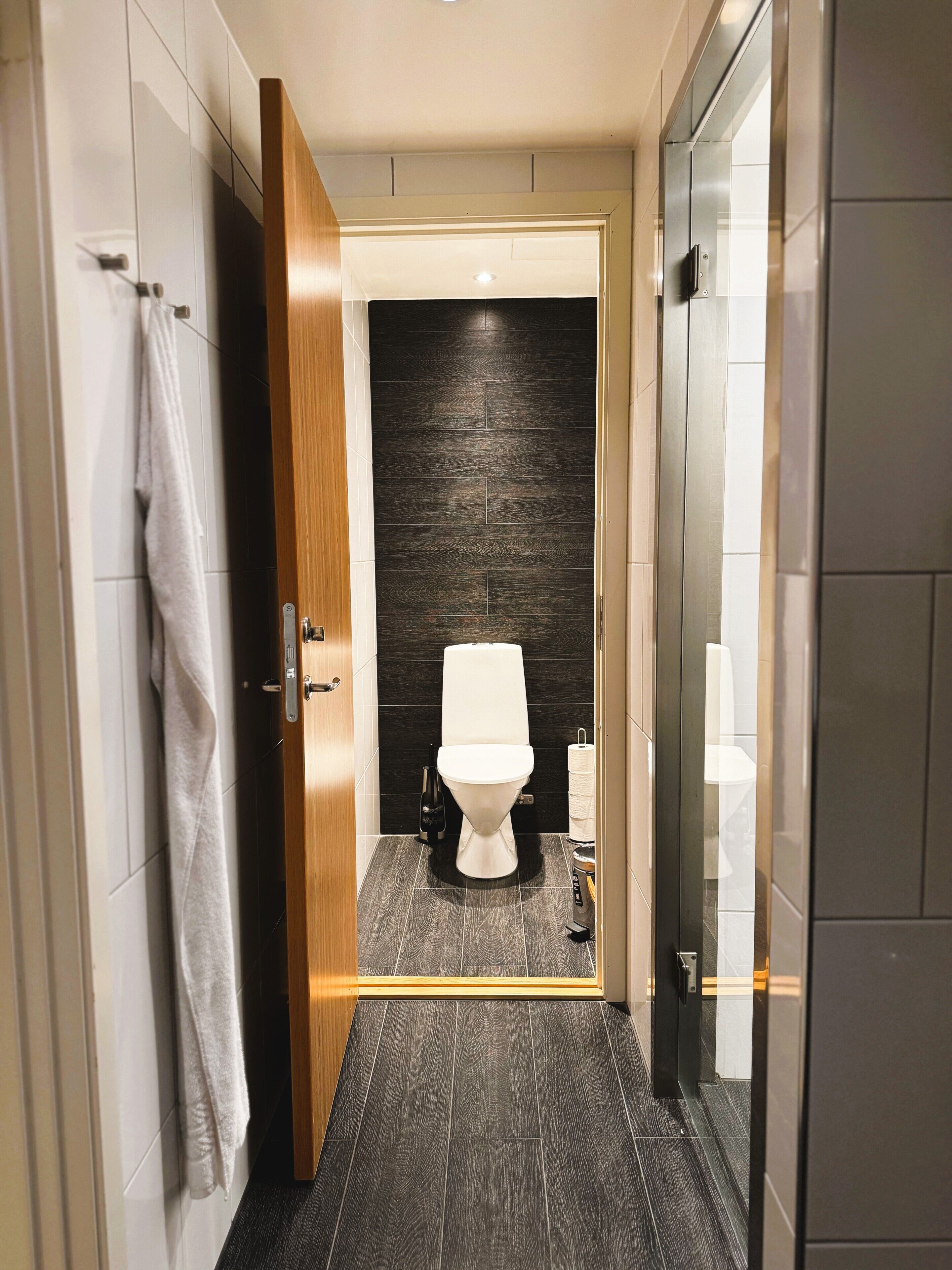 A modern bathroom with a dark wood floor, a white toilet, and a towel hanging on a rack.