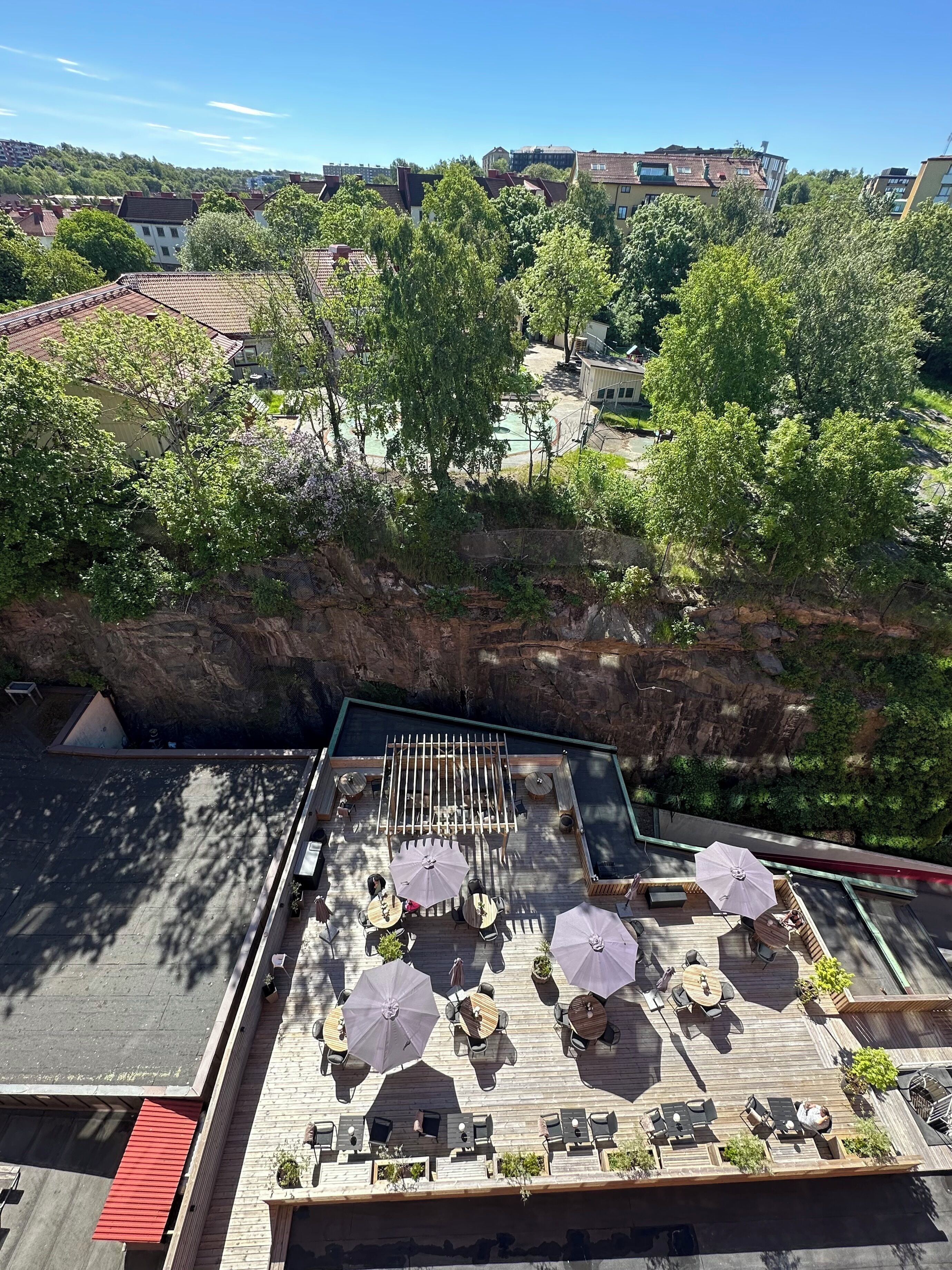 Een terras op het dak met buitenmeubilair, een zwembad en uitzicht op omliggende gebouwen en groen.