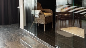 A modern interior with a glass partition, a wicker chair, a dining area, and a dark floor.