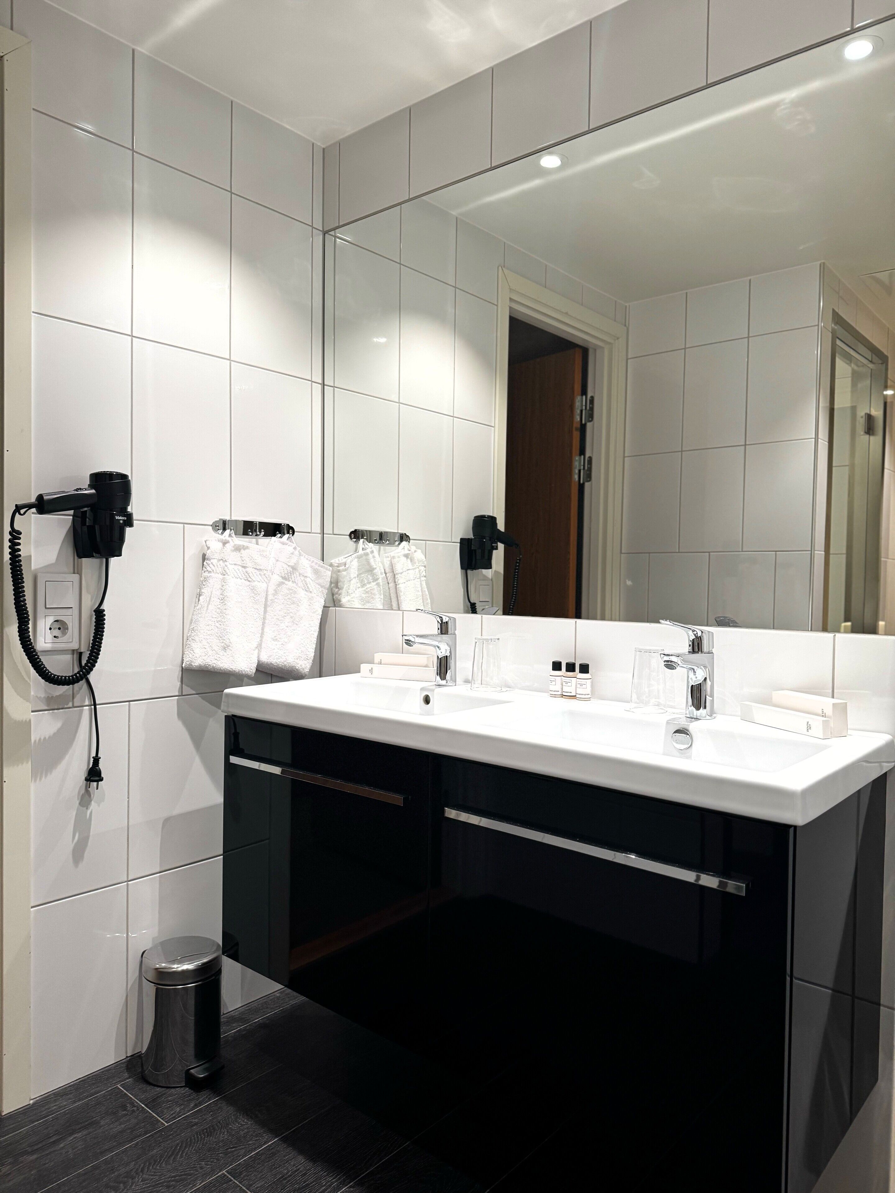 Un baño moderno con lavamanos doble, un espejo grande y un secador de pelo en la pared.