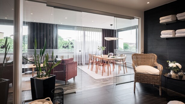 A modern living room with a dining area, large windows, and a view of greenery.