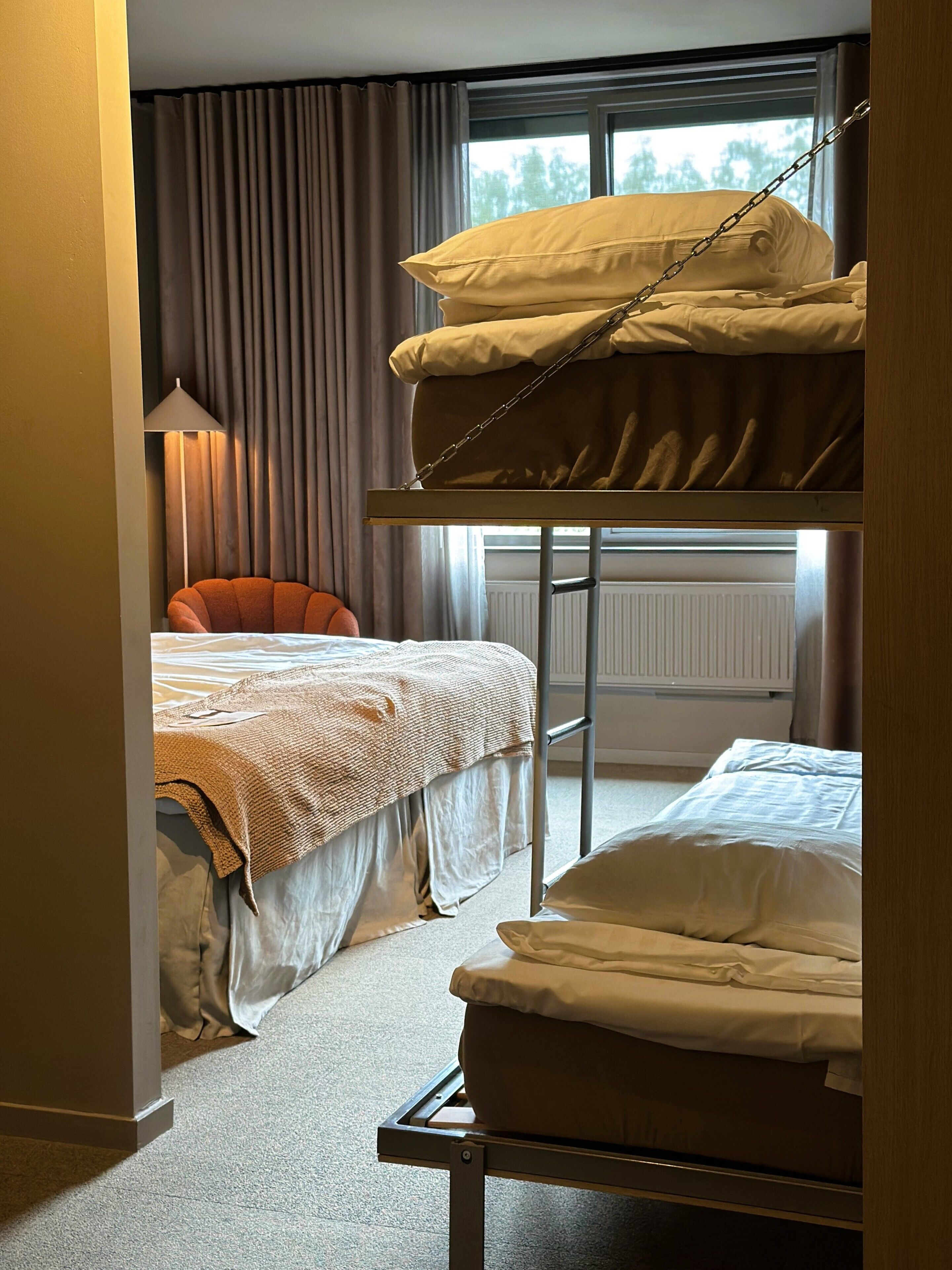 Una habitación con una cama litera, una cama individual, una silla y una lámpara.