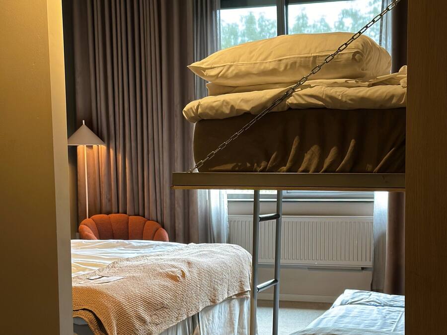 Una stanza con un letto a castello, un letto singolo, una sedia e una lampada.