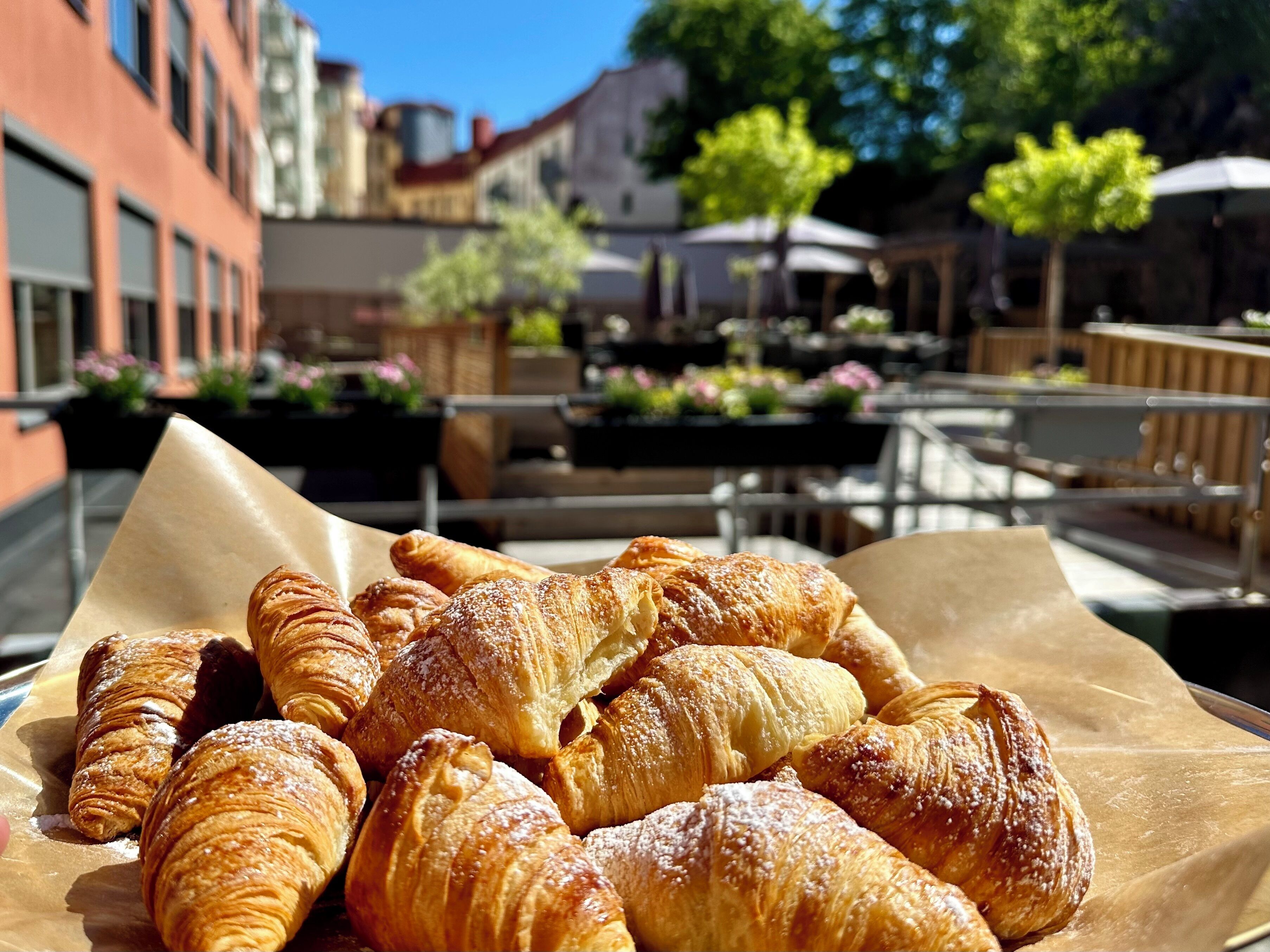 A variety of pastries on a table in an outdoor café setting with buildings and trees in the background.