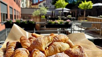 A variety of pastries on a table in an outdoor café setting with buildings and trees in the background.