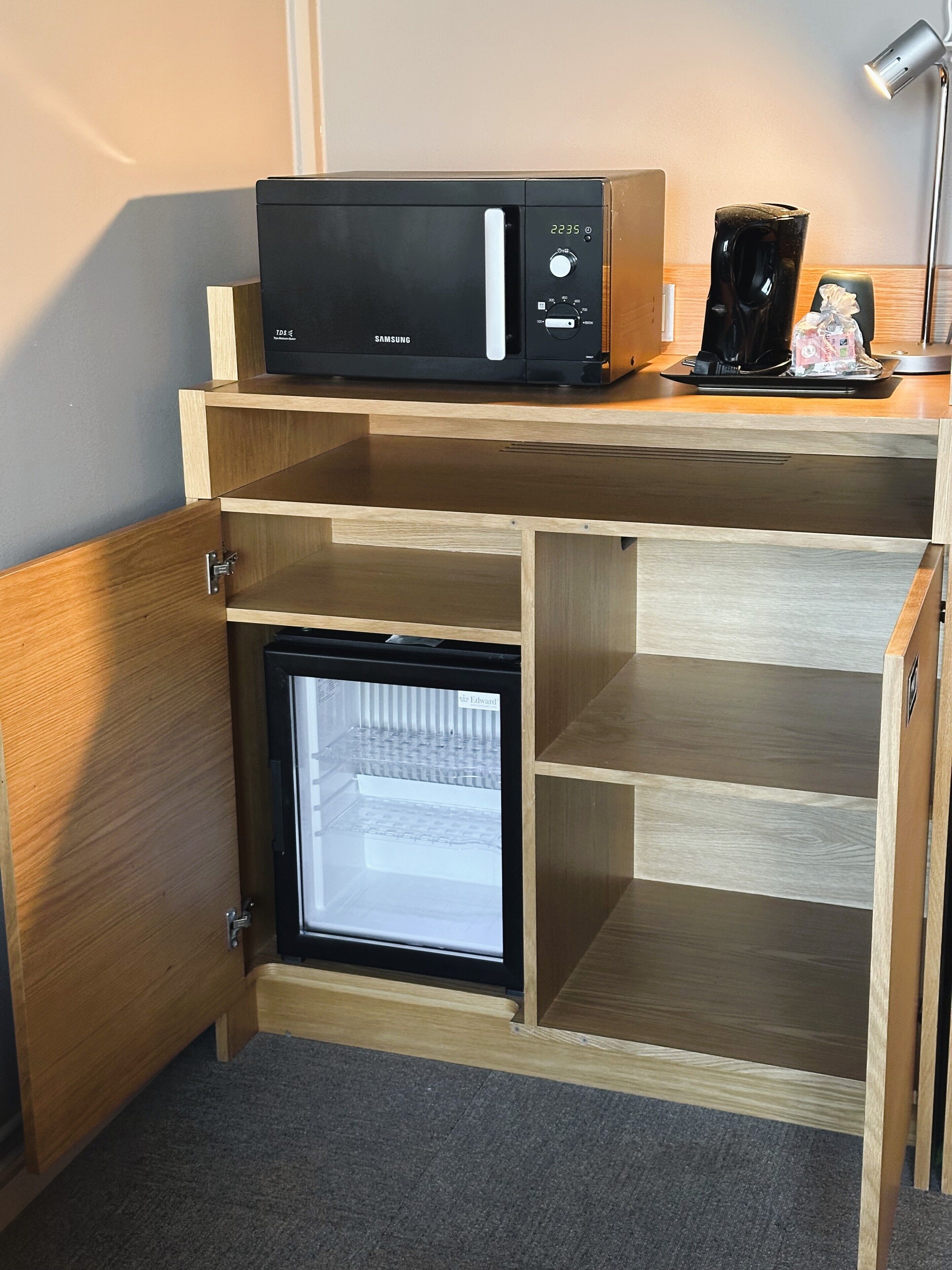 Una cocina compacta con microondas, un refrigerador pequeño y una cafetera sobre una encimera de madera.