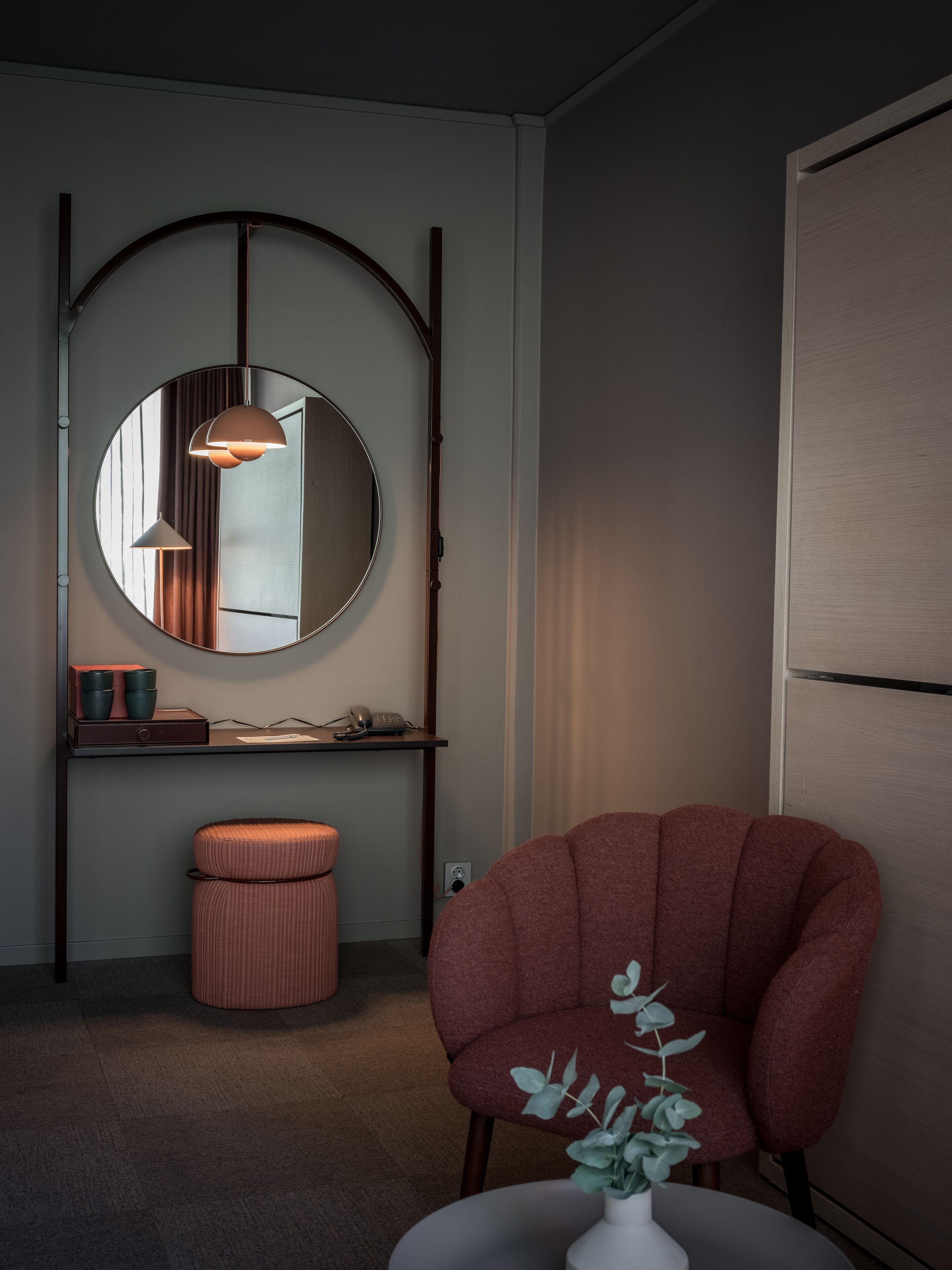 A modern room with a round mirror, a red armchair, and a small table with a plant.