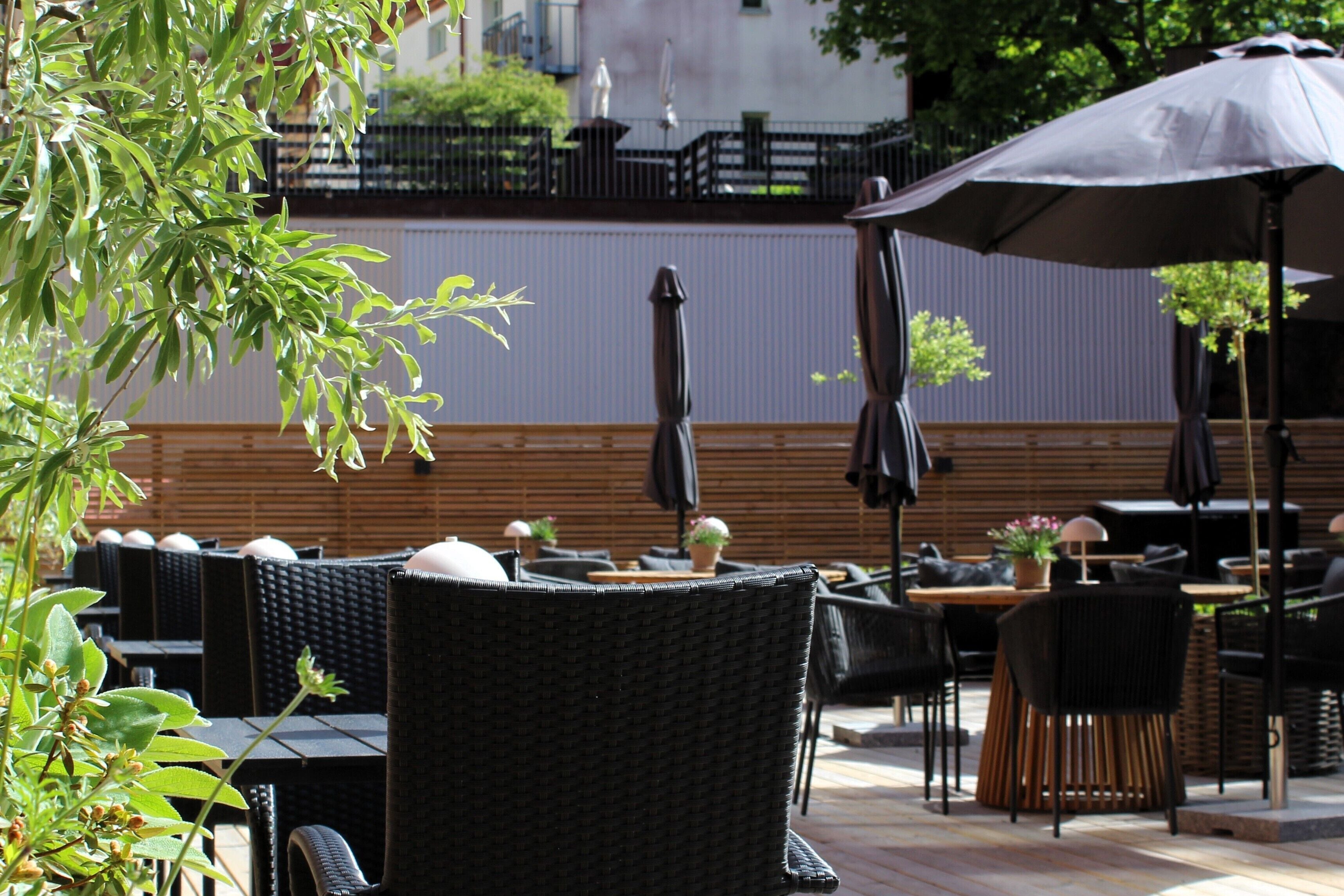 An outdoor seating area with wicker chairs and tables, umbrellas, and potted plants.