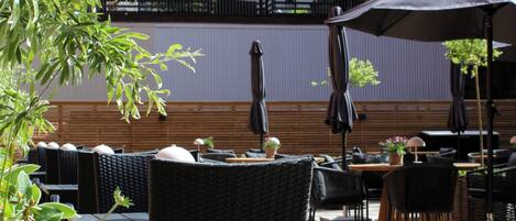 An outdoor seating area with wicker chairs and tables, umbrellas, and potted plants.