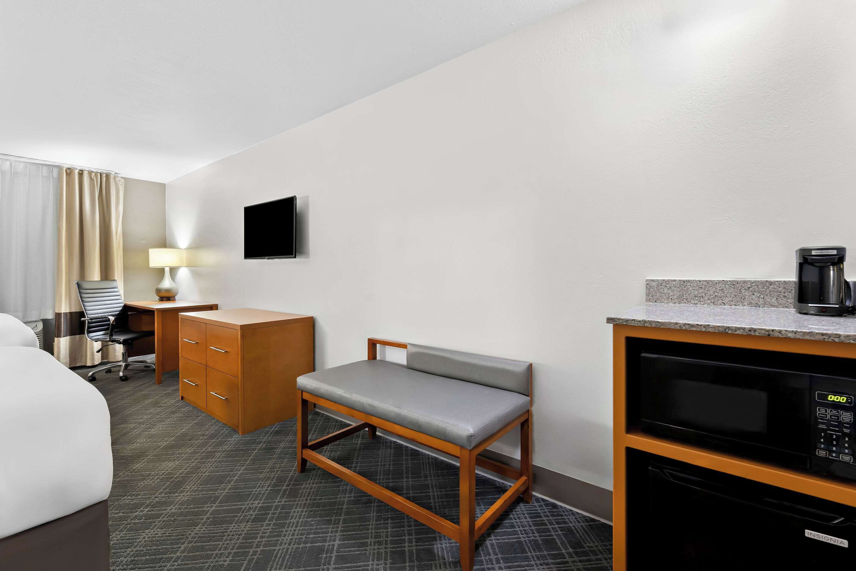 A hotel room with a bed, a desk with drawers, a chair, a television, a microwave, and a coffee maker.