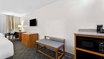 A hotel room with a bed, a desk with drawers, a chair, a television, a microwave, and a coffee maker.