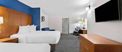 Habitación de hotel con dos camas, un escritorio, un aparador, un televisor y una puerta que da a otra habitación.