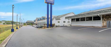 Un Comfort Inn & Suites con una carretera despejada, coches estacionados y un edificio de piedra al fondo.