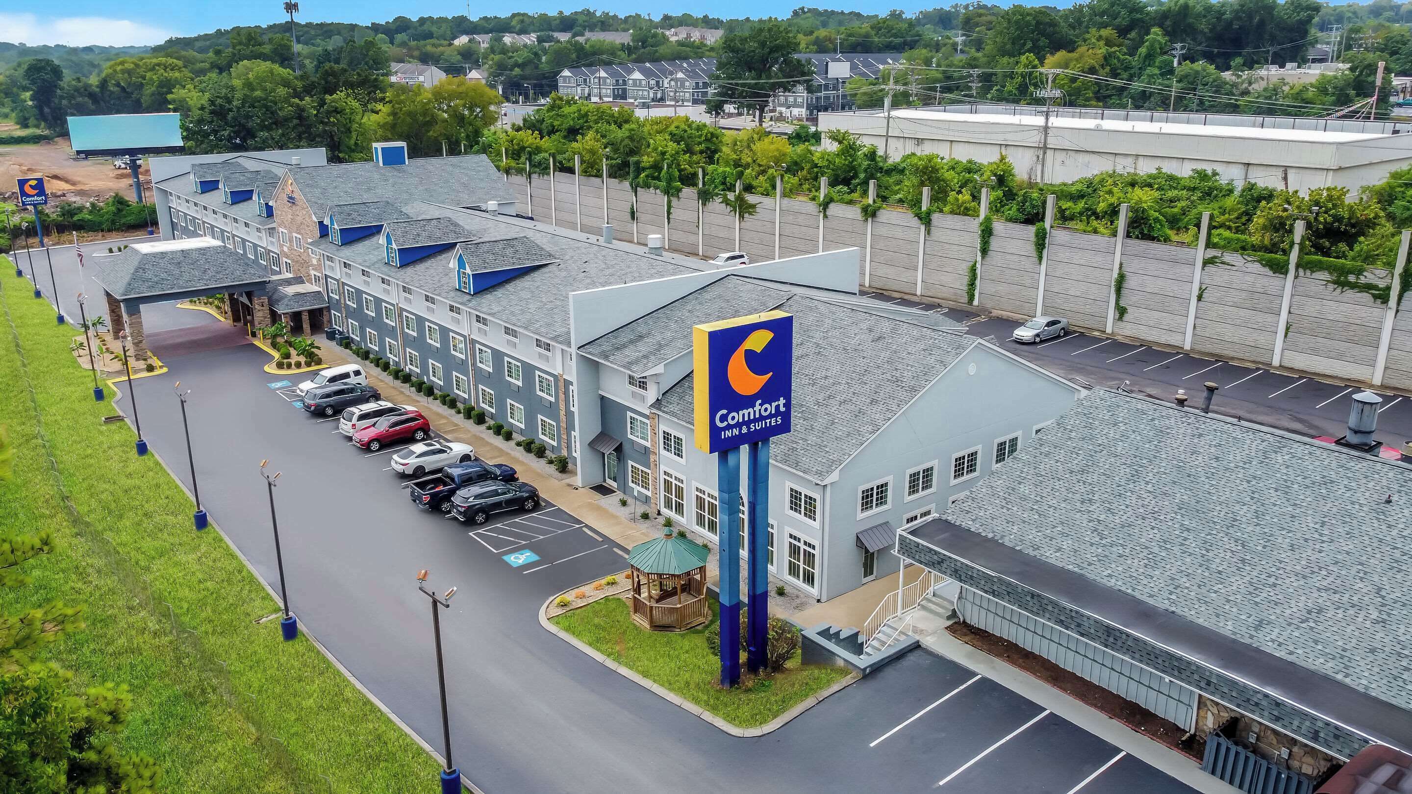 A Comfort Inn & Suites with a parking lot, a covered outdoor seating area, and a view of surrounding buildings and greenery.