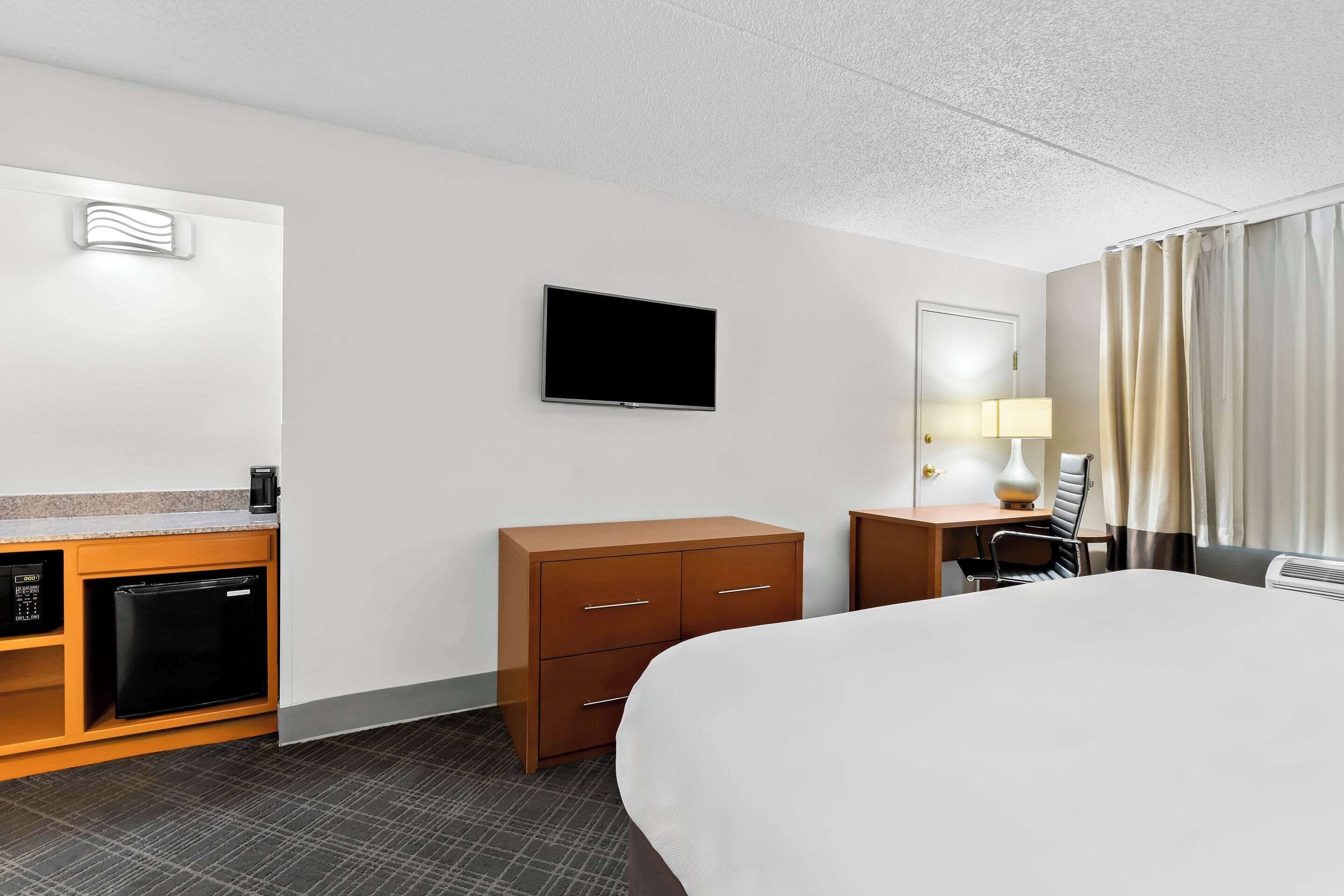 Una habitación de hotel con cama, escritorio con lámpara, televisión, minibar y puerta.