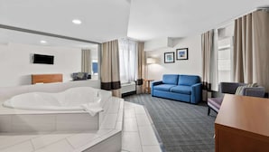 Ett hotellrum med ett stort badkar, en blå soffa, ett bord i trä och en platt-TV som är monterad på väggen.