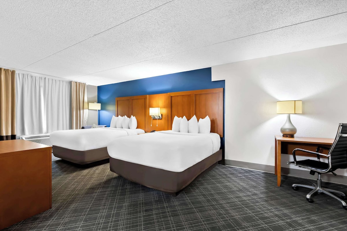 A hotel room with two beds, a desk, and a chair.
