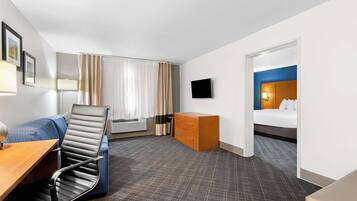 Habitación de hotel con escritorio, silla, cama, cómoda y televisión.