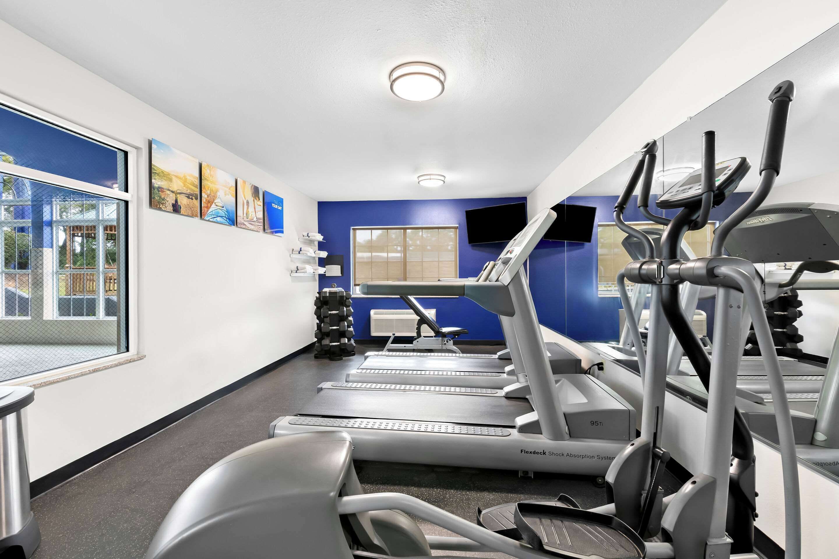 Un gimnasio con cintas de correr, elípticas y una banca para pesas.