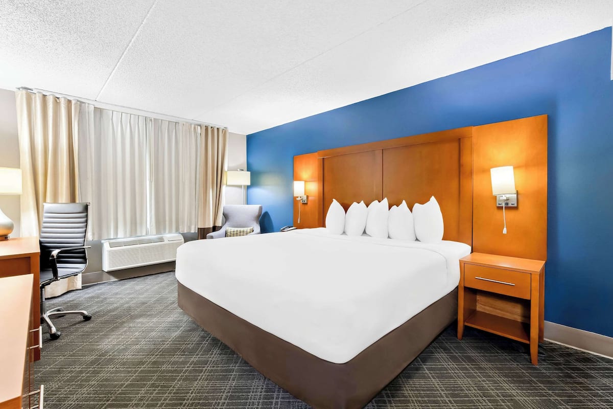 A hotel room with a large bed, a desk with a chair, a lamp, and a nightstand.