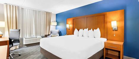 A hotel room with a large bed, a desk with a chair, a lamp, and a nightstand.