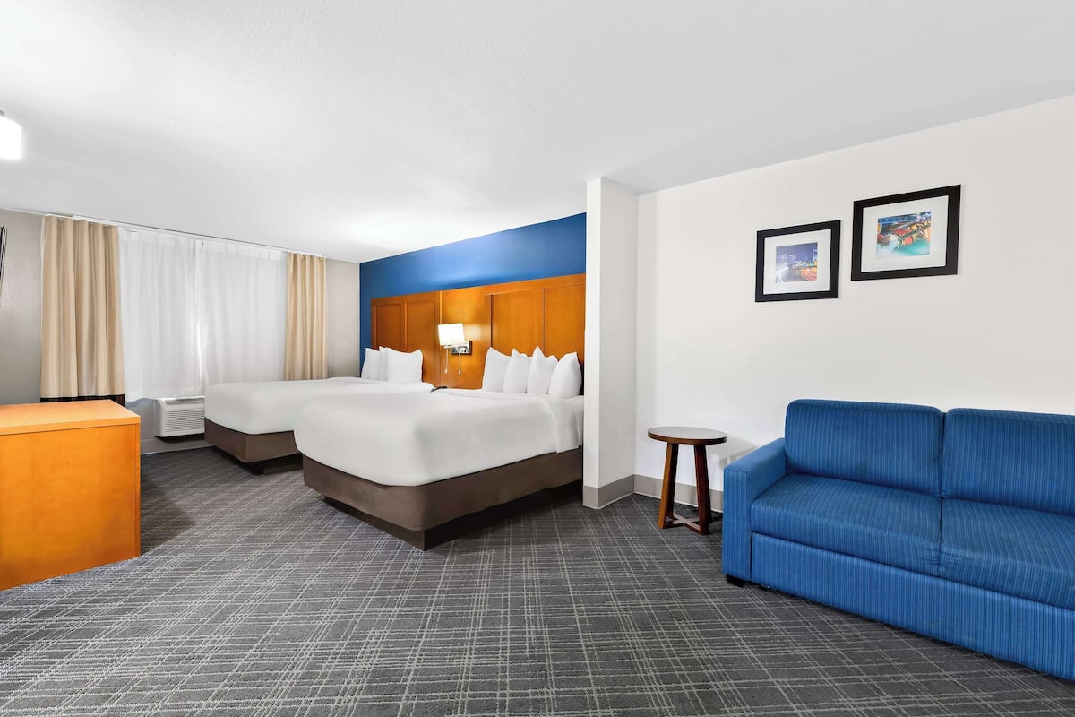 A hotel room with two beds, a blue sofa, a small table, and a wall-mounted lamp.
