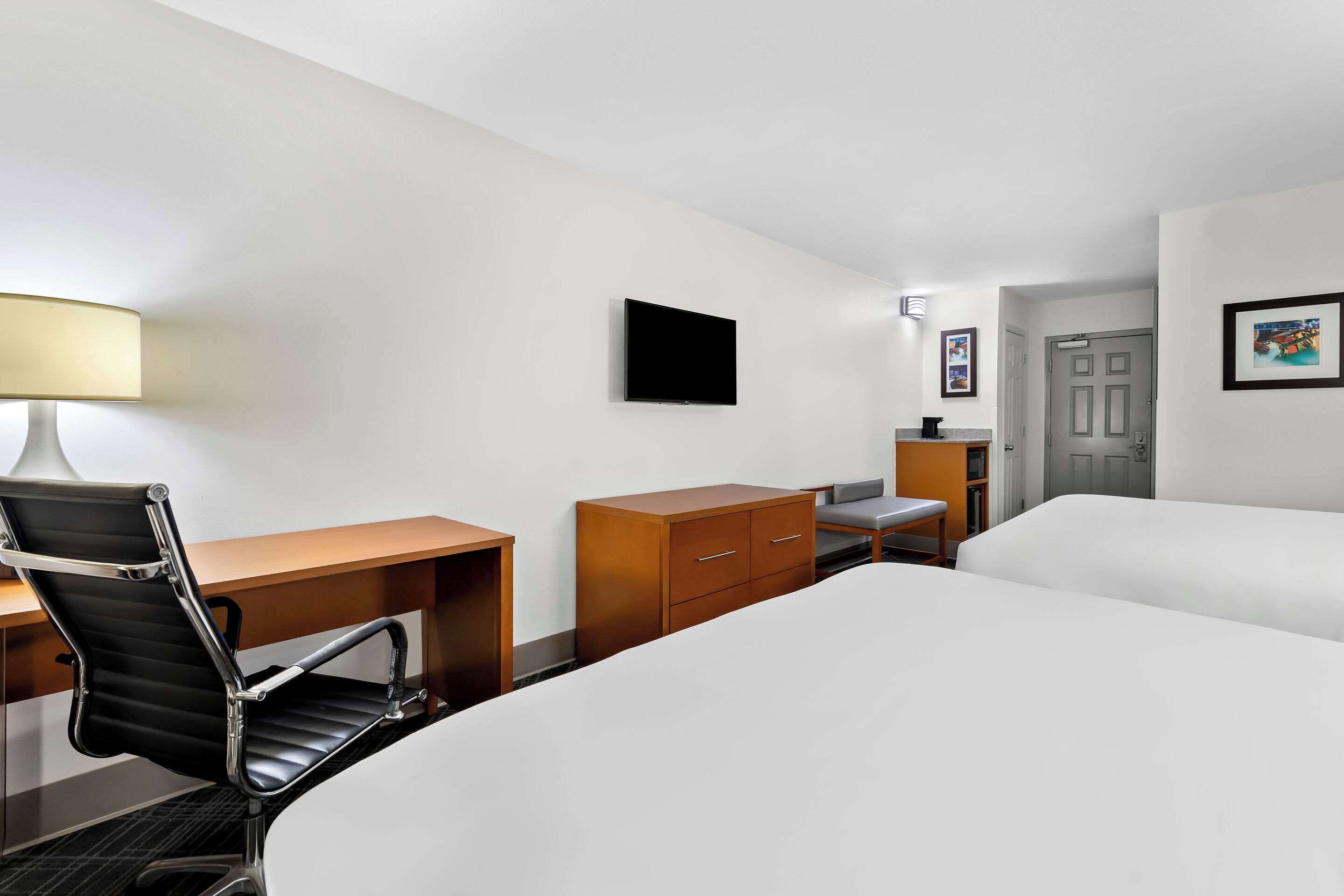 Una camera d'albergo con un letto, una scrivania con una sedia, un comò, una TV a schermo piatto e una porta.