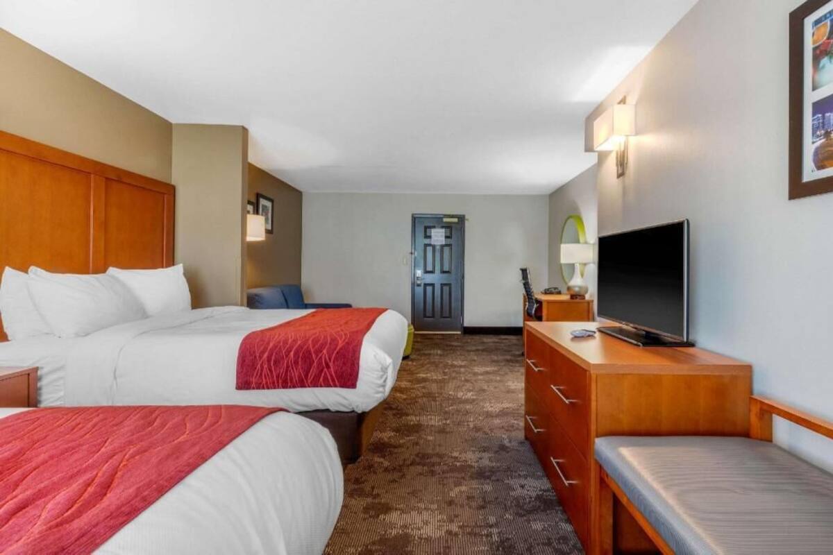 A hotel room with two beds, a TV, a desk, and a door in the background.