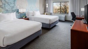 A hotel room with two beds, a desk, a chair, a TV, and a window with a view of trees.