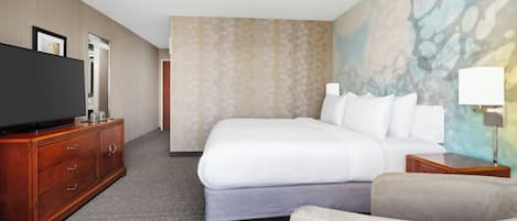 A hotel room with a large bed, a TV on a wooden dresser, a chair, and a painting on the wall.
