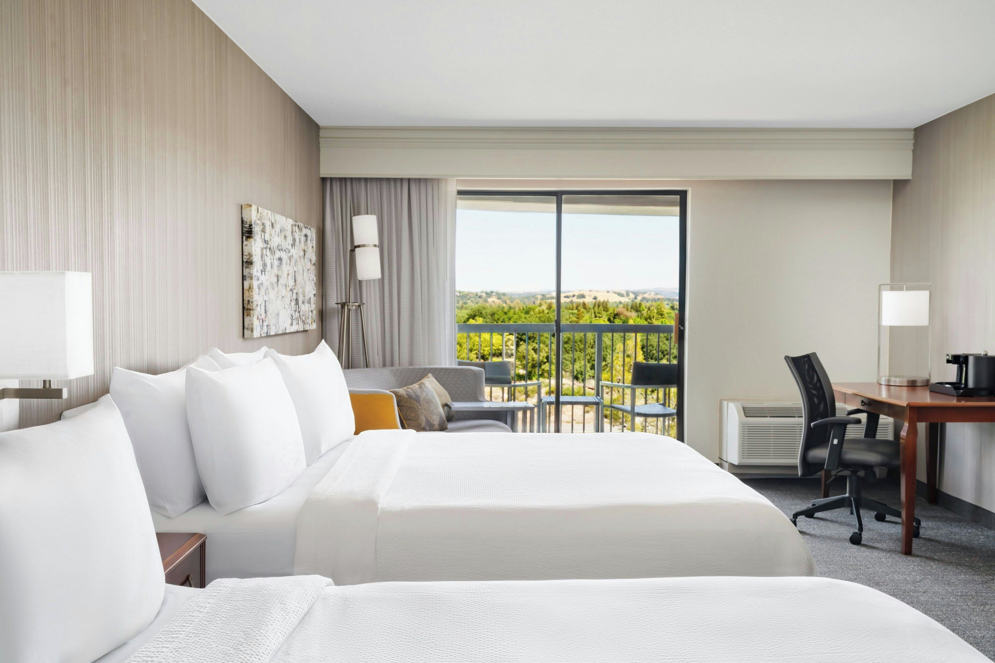 A hotel room with a large bed, a desk, a chair, and a view of the outdoors.