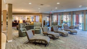 A spacious lobby with multiple seating areas, including sofas and lounge chairs, and large windows providing natural light.