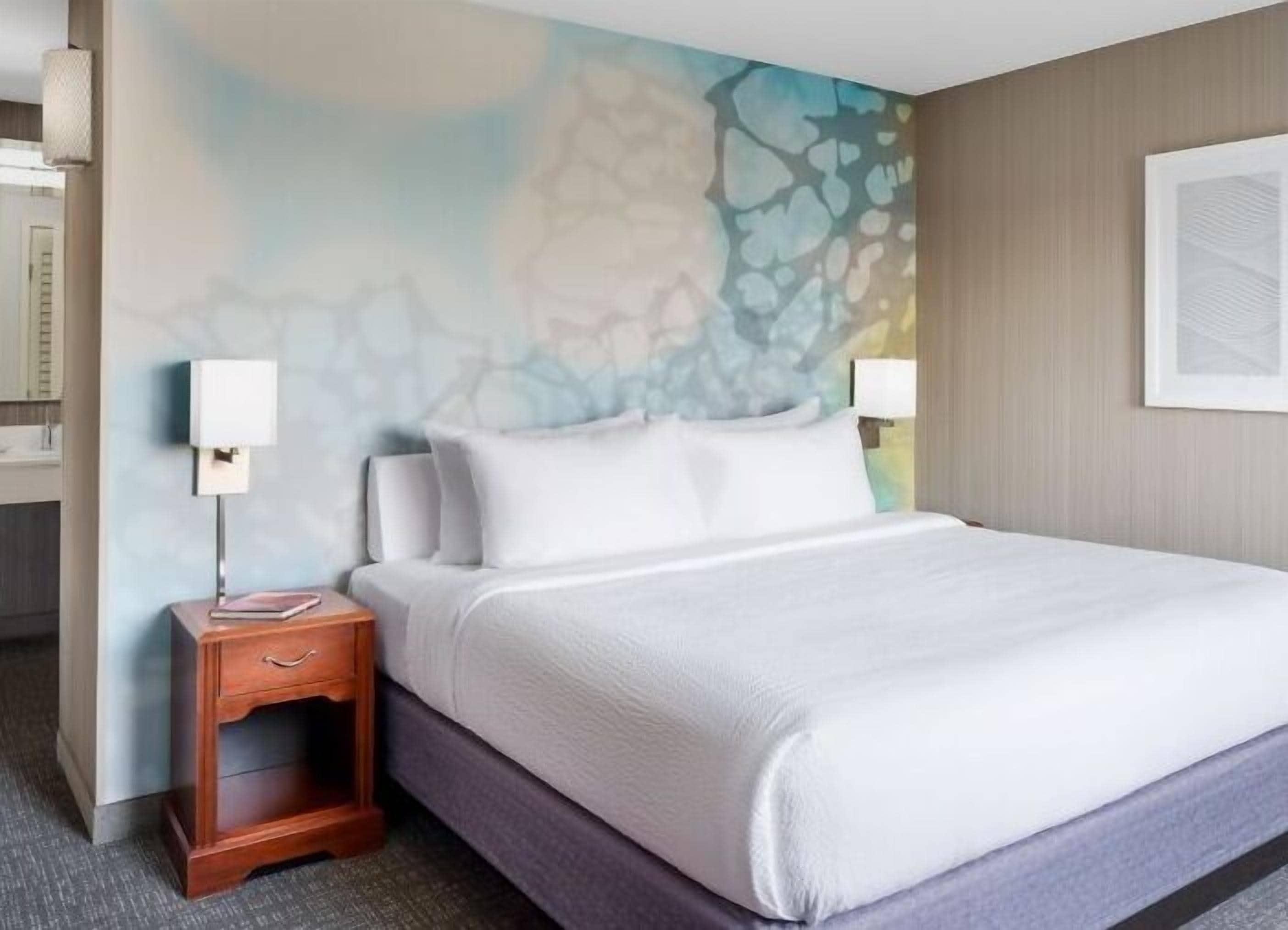 A hotel room with a bed, nightstand, and a wall with a textured design.