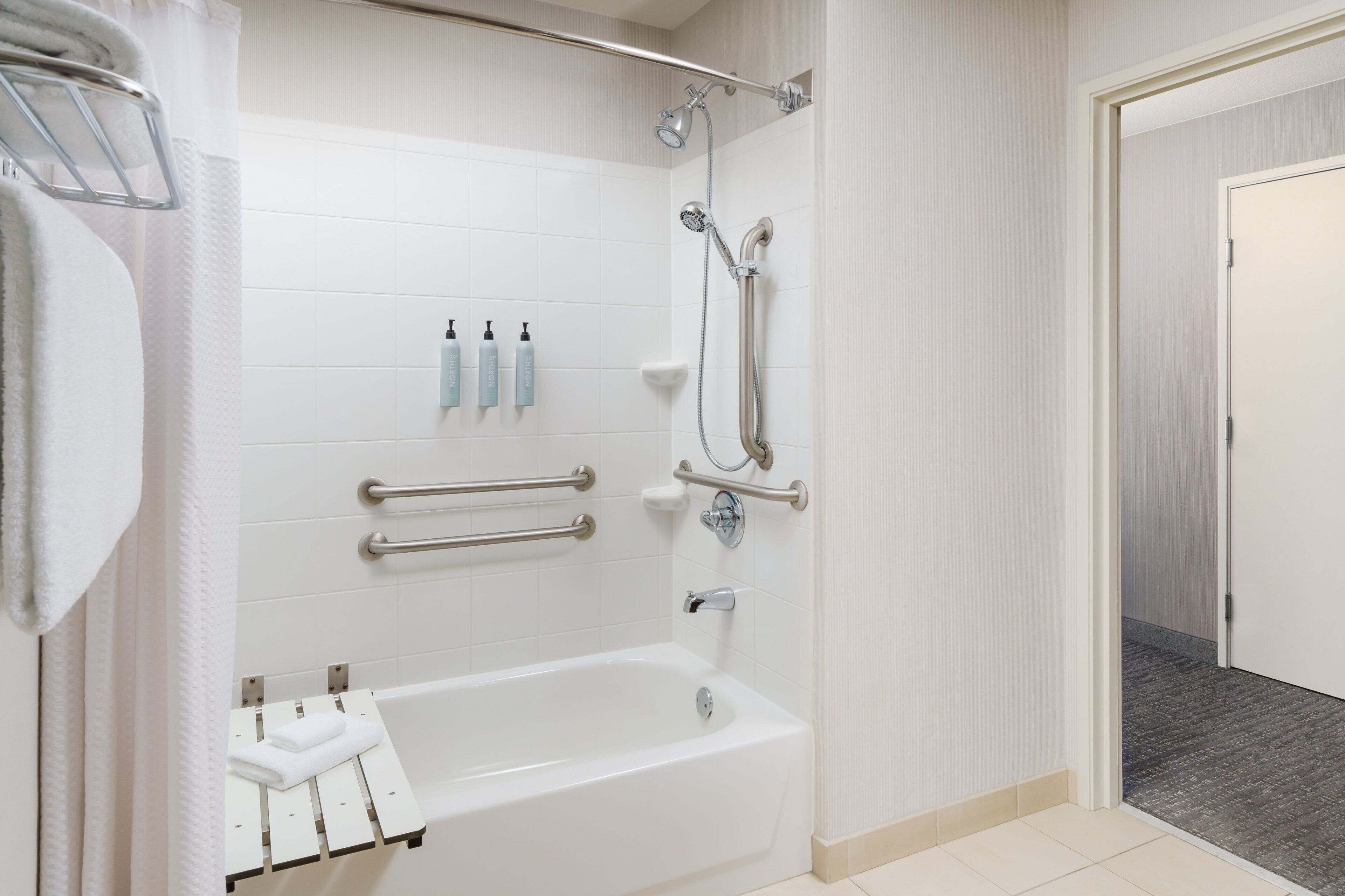 Une salle de bain moderne avec une baignoire blanche, des barres d’appui, une pomme de douche et un porte-serviettes.