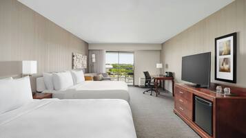A hotel room with two beds, a desk with a television, and a view of the outdoors.