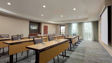 A conference room with multiple tables, chairs, and a large screen.