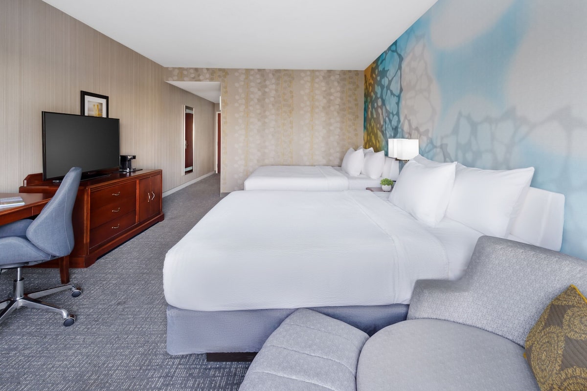 A hotel room with a large bed, a desk with a chair, a television, and a painting on the wall.