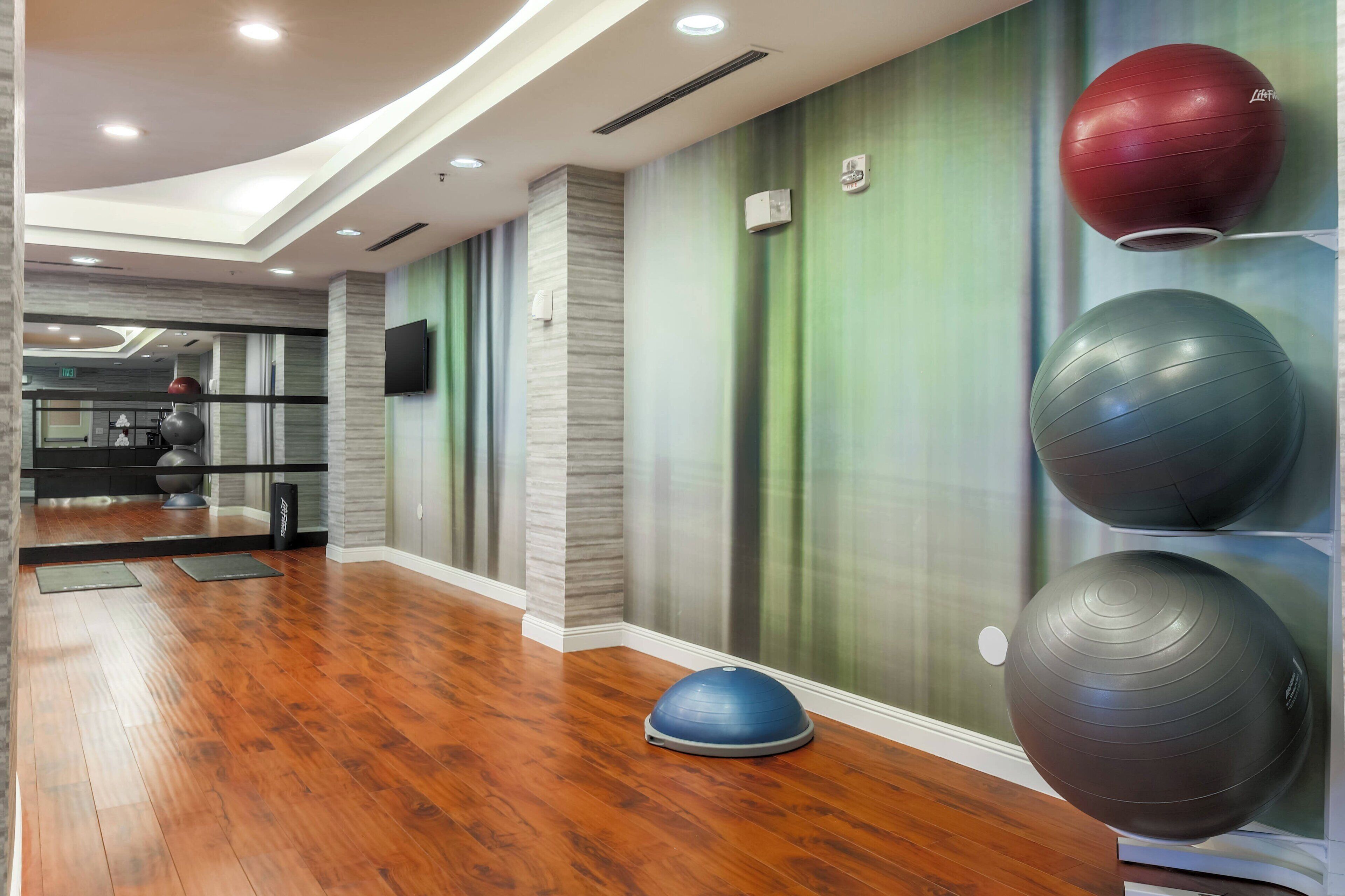 A gym with exercise balls, wooden flooring, and a mirror.
