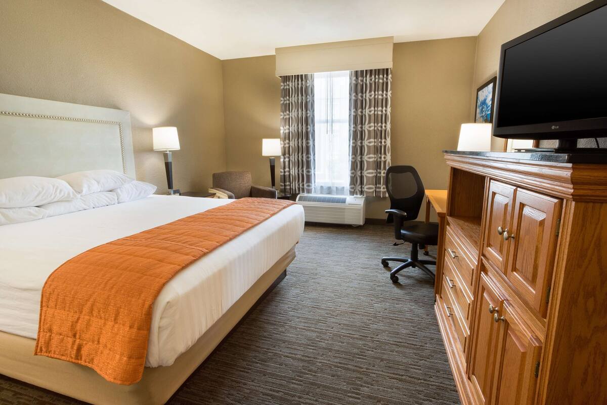 Habitación de hotel con una cama grande, un escritorio con silla, televisión y armario.