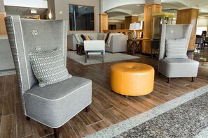 A modern lobby with grey upholstered armchairs, a round wooden ottoman, and a patterned rug. - Drury Inn & Suites Lafayette, LA (Lafayette)