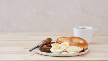 A plate with a bagel, sliced hard-boiled eggs, sausage links, and apple slices, accompanied by a white mug.